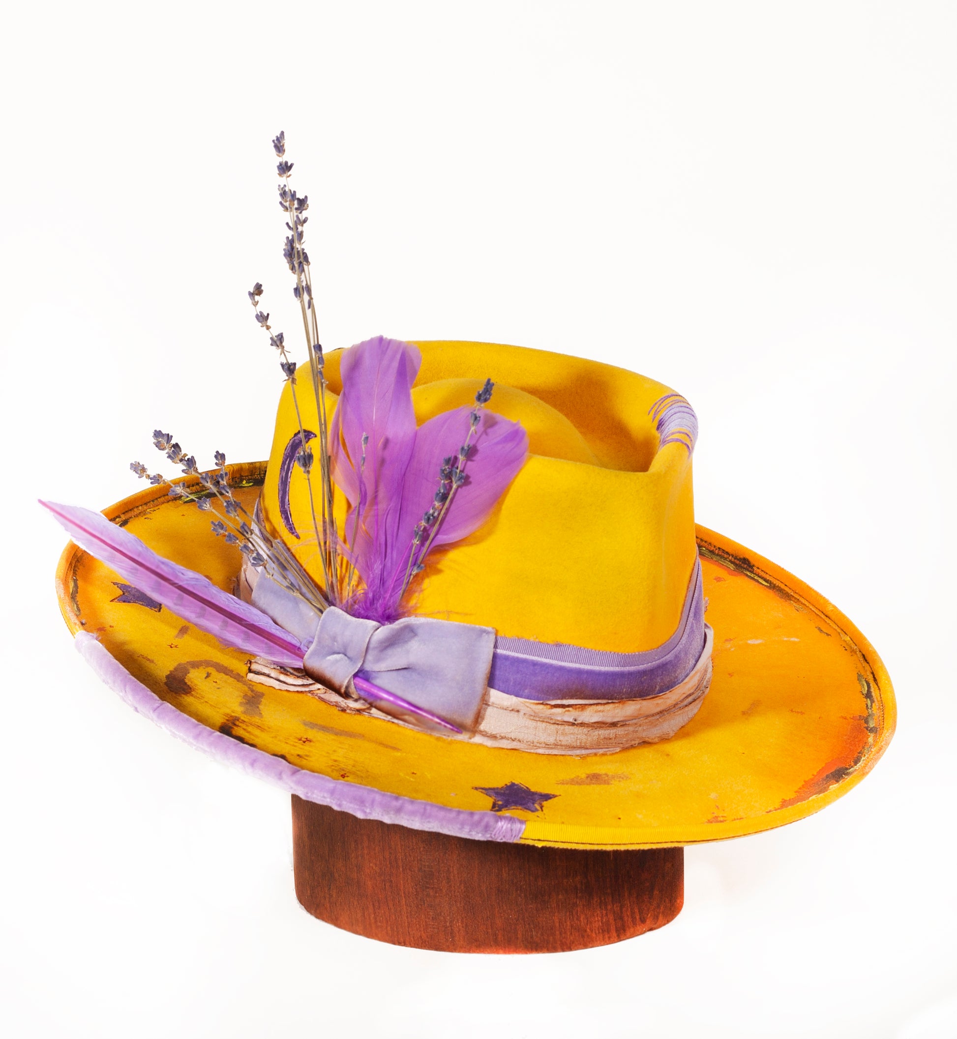 Mellow Yellow is a custom hat made from 100% beaver fur felt. It has a vintage hat band is hand painted and has a distressed handmade bohemian vibe. The hat is decorated with feathers and lavender. Also, a custom leather sweat band, branding and a silk hat lining.